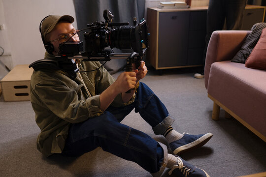 Male cameraman operates cinema camera sitting on the floor