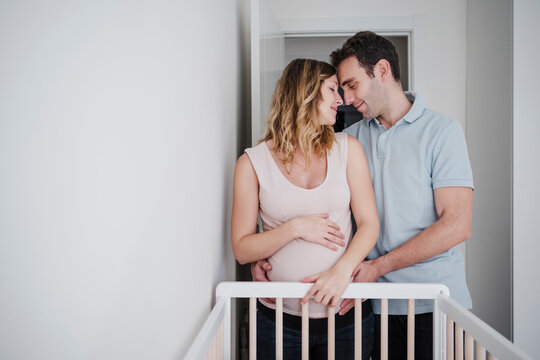 Romantic couple with face to face standing by crib at home