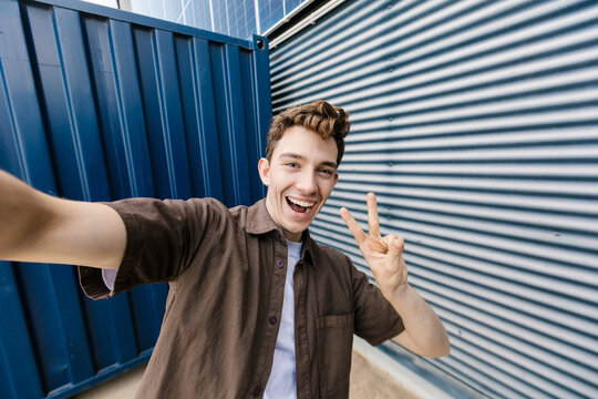 Young man takes a smiling selfie with a peace sign outdoors
