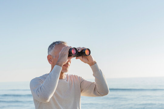Man looking through binoculars at beach