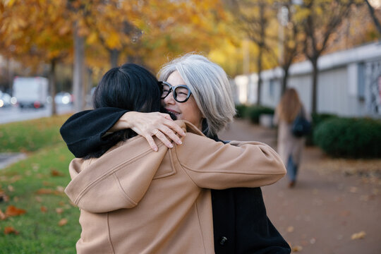 Smiling mother and daughter hugging on autumn city street