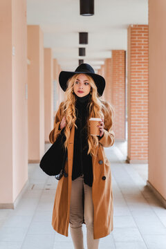 Woman in hat with coffee cup walking through corridor