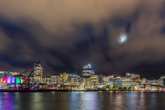 New Zealand, Wellington, Clouds over illuminated waterfront city skyline at night