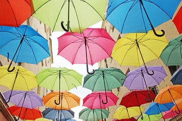 Obraz premium Colorful umbrellas hanging over a narrow city street against buildings.