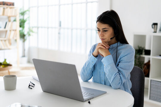 Businesswoman wearing headset using laptop while sitting with hand on chin at office