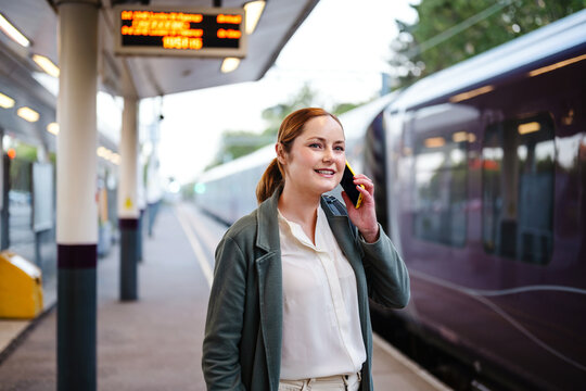 Smiling businesswoman talking on smartphone at train platform