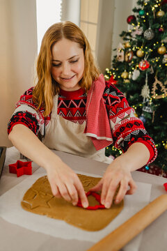 Smiling woman baking gingerbread cookies in festive kitchen at Christmas