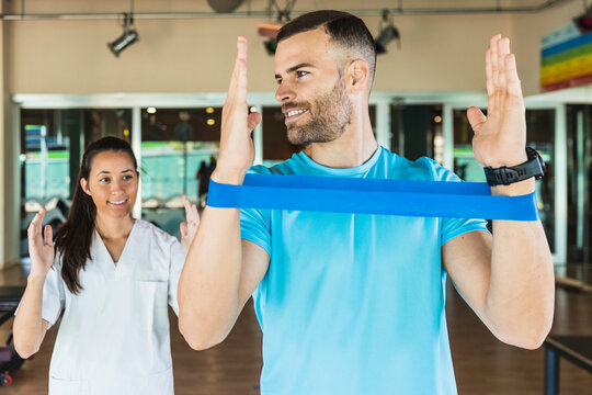 Sportsman listening to fitness instructor guiding from behind at gym