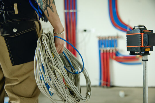 Cropped shot of young adult electrician holding ethernet cables during house renovation with laser level in foreground, representing smart home installation services