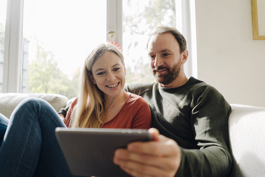 Couple sitting at home on couch, using digital tablet
