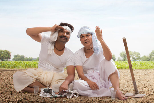 Two farmers sitting in field drinking tea and eating snacks