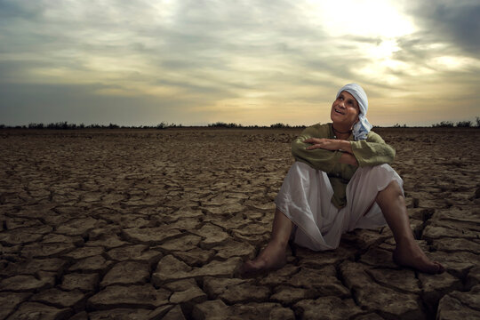 Senior farmer looking at sky sitting in drought hit field