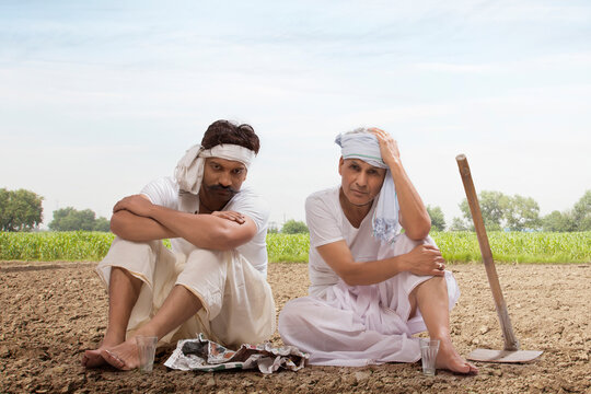 Tensed two farmers sitting in field drinking tea and eating snacks