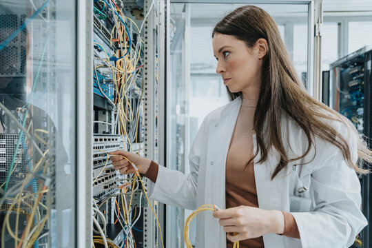 Young woman plugging transceiver on fiber optic cable in data center