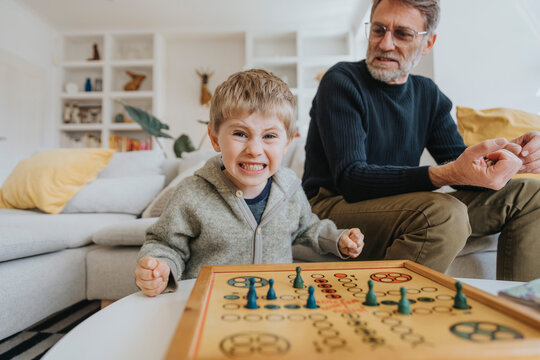 Son clenching teeth and fists while father sitting on sofa in background at home