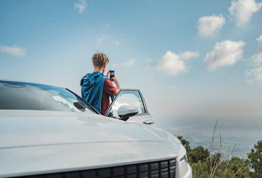 Man photographing with mobile phone standing by white car