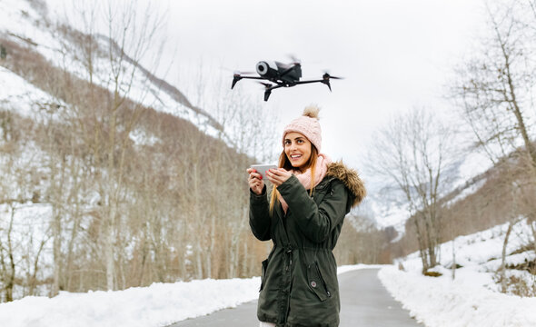 Spain, Asturias, young woman navigating a drone in the snowy mountains