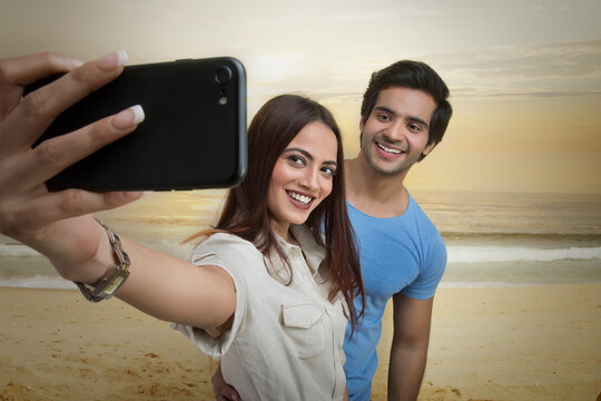 Smiling couple taking selfie on beach at sunset