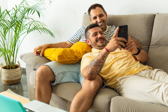 Gay couple relaxing on sofa watching smartphone