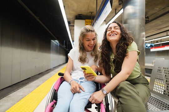 A woman in a wheelchair and a friend laugh at a smartphone