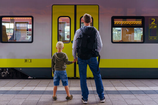 Father holding hands with son standing in front of train