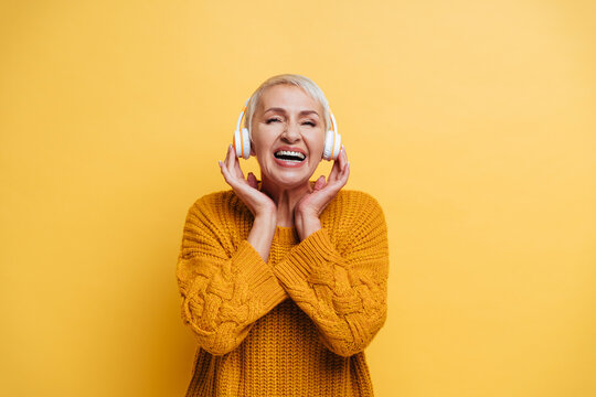 Smiling woman wearing headphones standing against yellow background