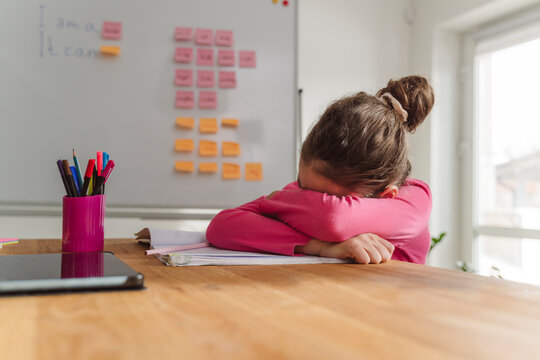 Girl crying over book on table at home