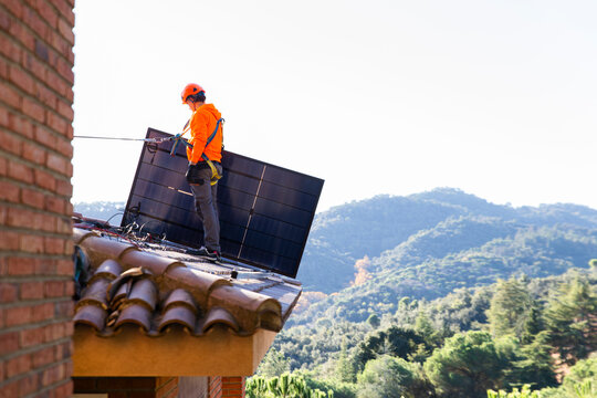 Worker installing solar panel on roof in Barcelona mountain area