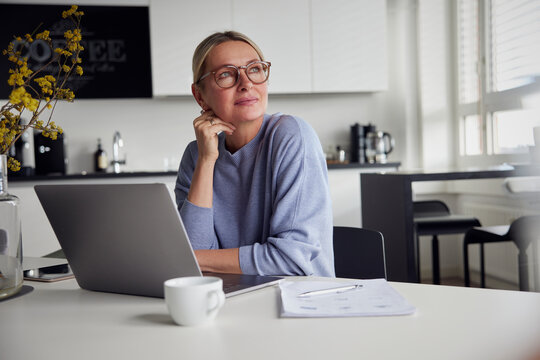 Thoughtful businesswoman wearing eyeglasses sitting with laptop at table