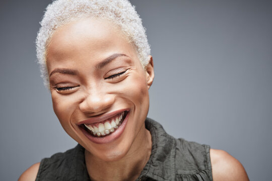 Portrait of laughing woman with eyes closed in front of grey background