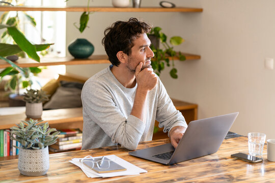 Contemplating freelance worker looking away while sitting with laptop at home office