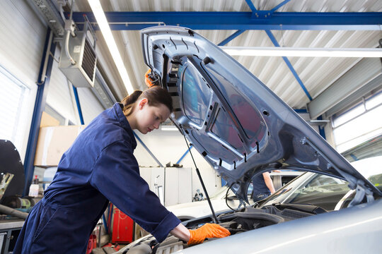 Young woman working in repair garage, checking engine