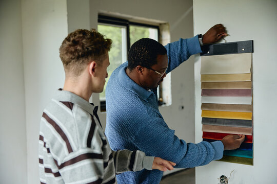 African American interior designer and young adult Caucasian client choosing fabric color palette in house under renovation, promoting home improvement services