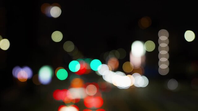 歩道橋から見下ろす夜の幹線道路と丸くぼやけた車や街の灯り。赤から青に変わる信号