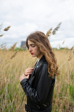 A young woman wears a leather jacket in a field of reeds