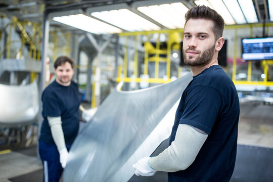 Two colleagues carrying bonnet in car factory