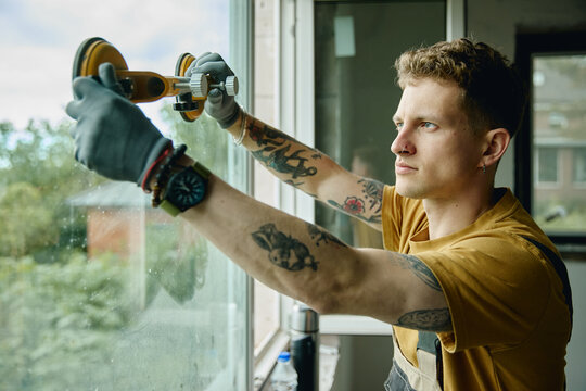 Young adult Caucasian male worker installing glass window pane using suction cups during house renovation. Image suitable for home improvement services and construction marketing