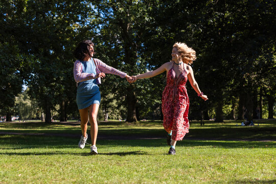 Happy women hold hands while running in a sunny park
