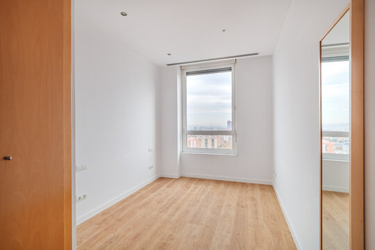 Empty bright room with light oak wooden floor, large window, white walls and tall wall mirror, creating minimalist interior with spacious modern residential feel