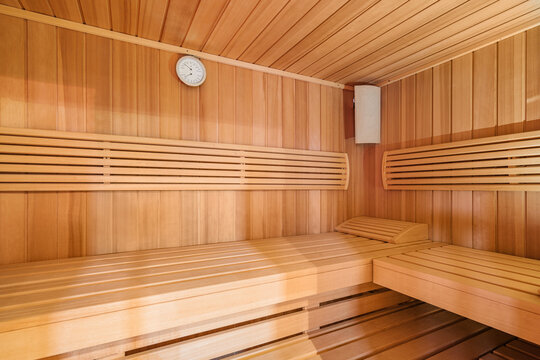 Wooden sauna interior with tiered benches, round wall clock, slatted timber walls, and warm amber light creating calm wellness retreat for relaxation, comfort, and serene spa atmosphere