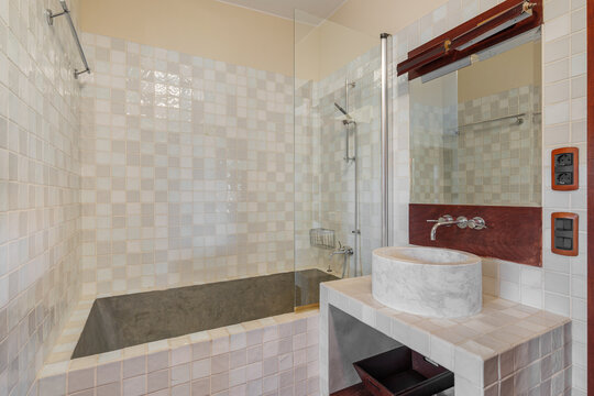 Contemporary bathroom interior featuring large built-in bathtub, tiled surround, modern vanity mirror, countertop basin, neutral tones, bright lighting, and spacious clean design