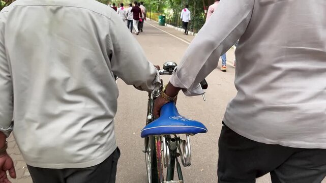 Rear view of two friends walking together while pushing a bicycle along a quiet road, capturing companionship, leisure and everyday life
