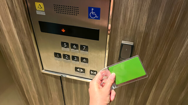 A hand swipes an RFID access card at a reader next to a stainless steel elevator control panel with Braille buttons. A concept for secure access and entry control in a residential condominium.