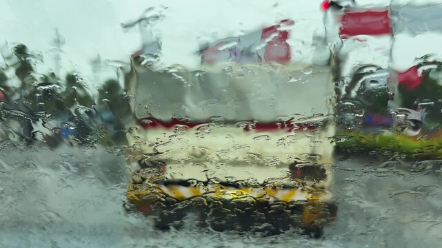 View through a wet car windshield during a downpour, with blurred traffic and water droplets creating a moody driving scene and reduced visibility	