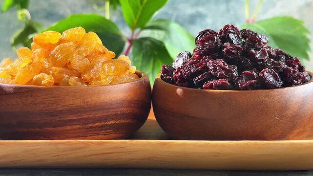 Close up of three raisin varieties in wooden bowls with grape leaves during a smooth leftward camera movement