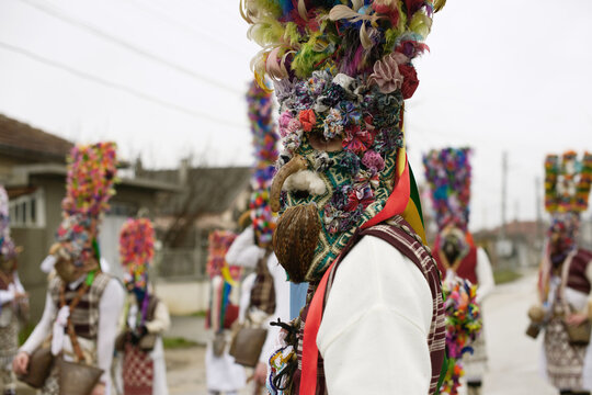 Grebentsi kukeri performer with rooster-skin beard, horse-tail hair, decorated headpiece, ribbons and bells.