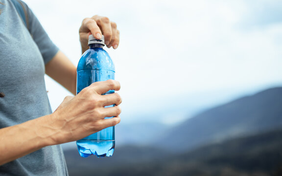 Close Up Of Woman Opening Drinking Water Bottle During Outdoor Hike To Stay Hydrated In Summer Heat
