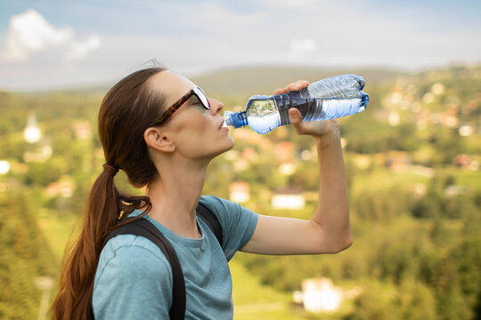Woman Drinking Water Outdoors During Summer Hike to Stay Hydrated in Hot Weather
