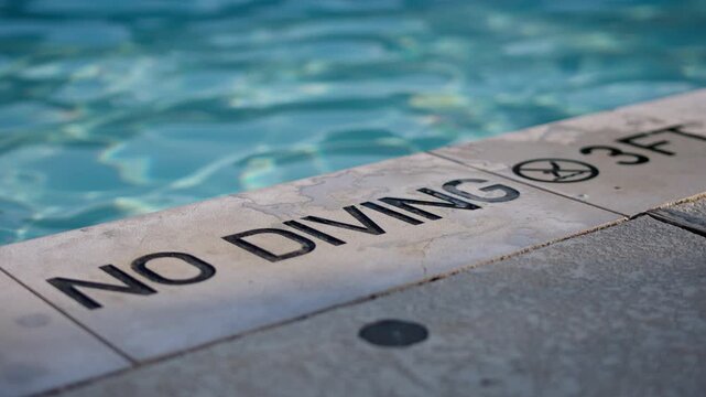 No diving sign on the edge of a swimming pool, water ripples in the background