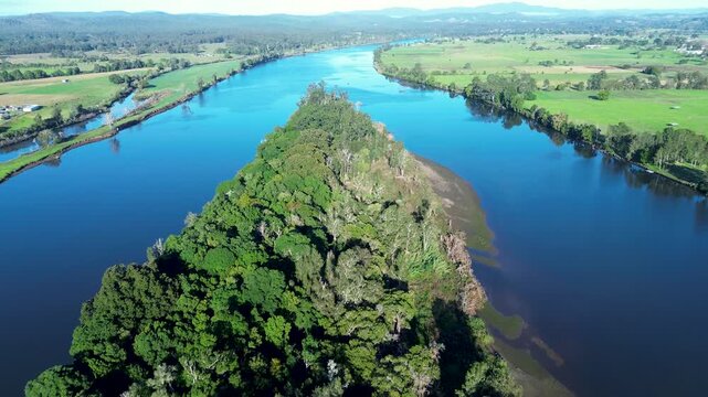 Drone aerial landscape of Coocumbac Island Nature Reserve covered in woodland forest tree canopy along the Manning River with the rural countryside of Taree on the Mid North Coast of Australia tourism